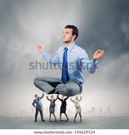 Young businessman sitting in lotus pose and supported by colleagues