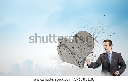 Young businessman breaking stone heart with punch