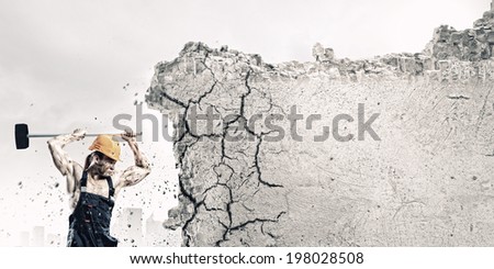 Strong man in uniform breaking brick wall with hammer