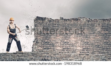 Strong man in uniform breaking brick wall with hammer