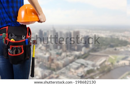 Close up of woman mechanic with yellow helmet in hand against city background