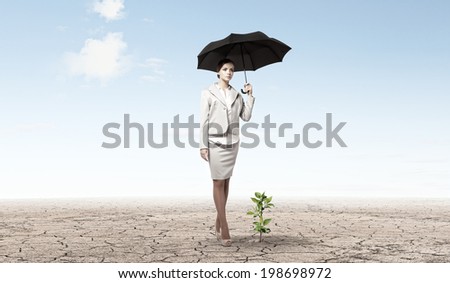 Attractive businesswoman protecting green sprout with umbrella