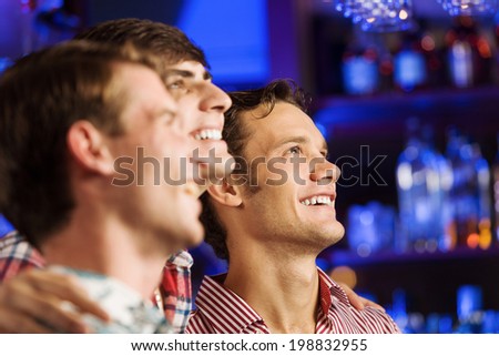 Three young men at bar watching match and shouting