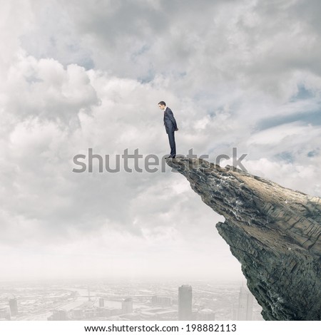 Young businessman standing on edge of rock mountain Young businessman standing on edge of rock mountain
