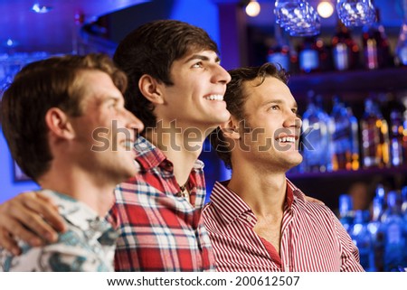 Three young men at bar watching match and shouting