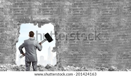 Young businessman with big hammer against wall