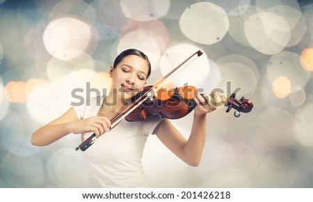 Young attractive woman playing violin with bokeh lights at background