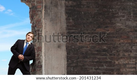Young businessman making effort to move brick wall