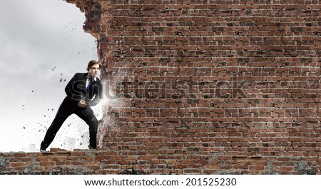 Young businessman making effort to move brick wall