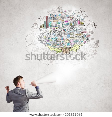 Young businessman speaking in trumpet with business sketches on wall