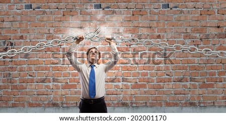 Young furious businessman breaking metal chain with hands
