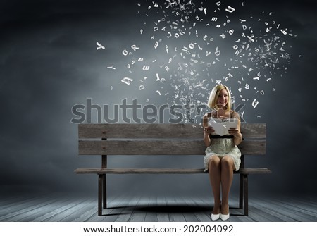 Young pretty woman sitting on bench and reading book