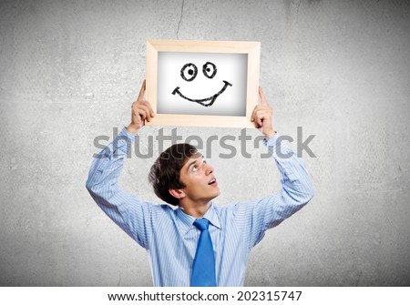 Young happy businessman holding frame with drawn smile