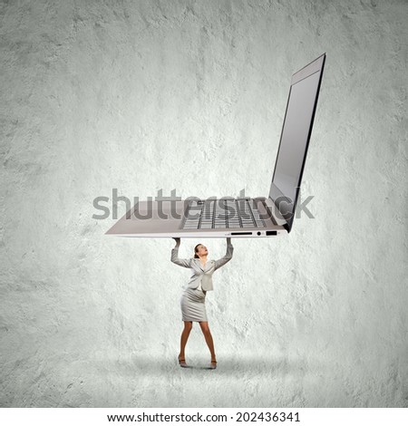 Young businesswoman lifting huge laptop above head