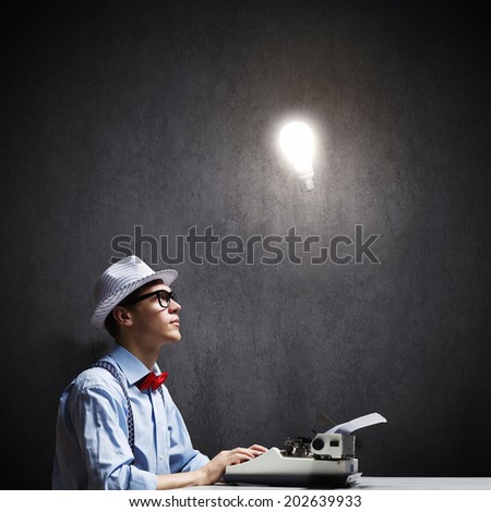 Young funny man in glasses writing on typewriter