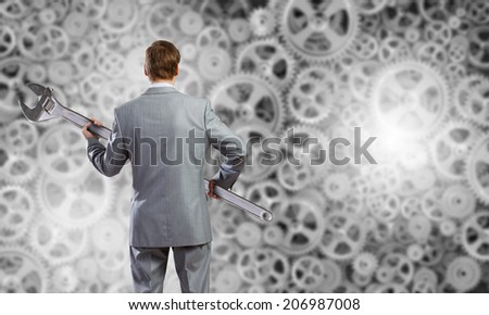 Rear view of determined businessman with wrench in hands and cogwheels at background