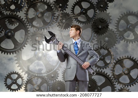 Young determined businessman with wrench in hands and cogwheels at background