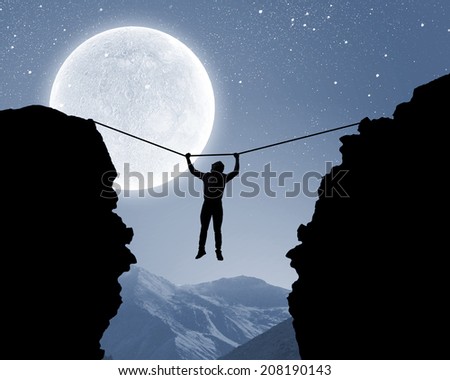 Silhouette of man hanging on rope above mountain gap