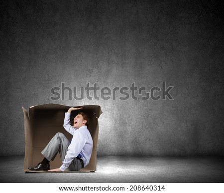 Young frustrated businessman trapped in small carton box