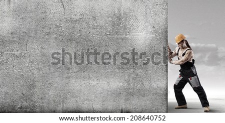 Strong man in uniform and helmet pushing wall. Place for text