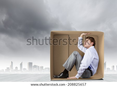 Young frustrated businessman trapped in small carton box