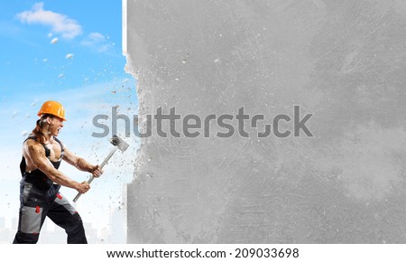 Strong man in uniform breaking wall with hammer
