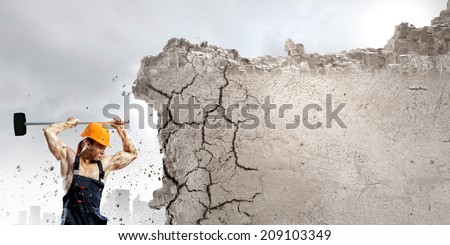 Strong man in uniform breaking wall with hammer