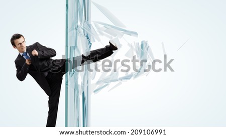 Young determined businessman breaking glass with karate kick