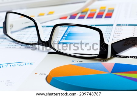Eye glasses lying on papers with graphs and diagrams
