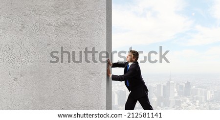 Young businessman making effort to move stone wall