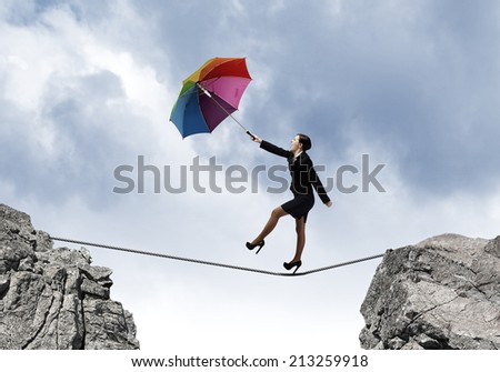 Young businesswoman walking on rope above gap with colorful umbrella