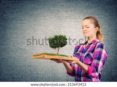 Young woman in casual holding opened book with green tree