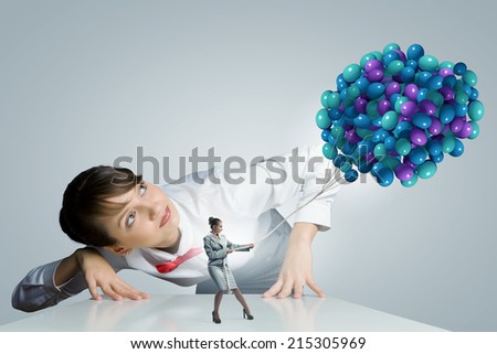 Businesswoman looking at businesswoman miniature pulling bunch of balloons