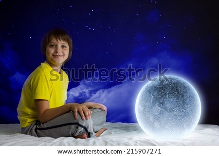 Cute boy sitting in bed and dreaming about moon