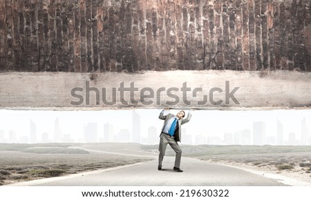 Young powerful businessman lifting brick wall above head