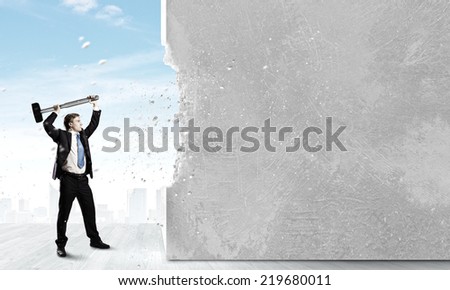 Young determined businessman crashing wall with hammer