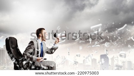 Young angry businessman sitting on chair and screaming in megaphone