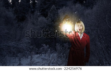 Young blonde in red cloak with lantern in night forest