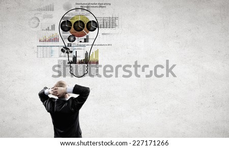 Rear view of businessman looking thoughtfully at business sketches