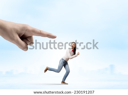 Young woman in casual running away from big hand