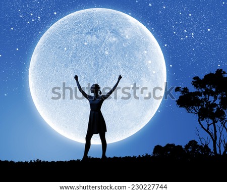 Silhouette of woman against full moon with hands up