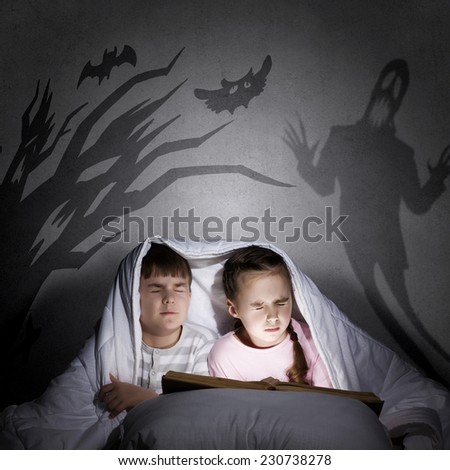 Two little kids reading book under blanket