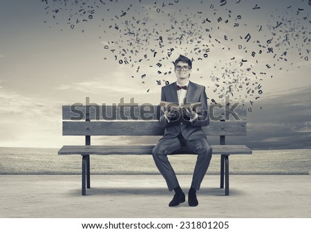 Young man in suit sitting on bench with book in hands