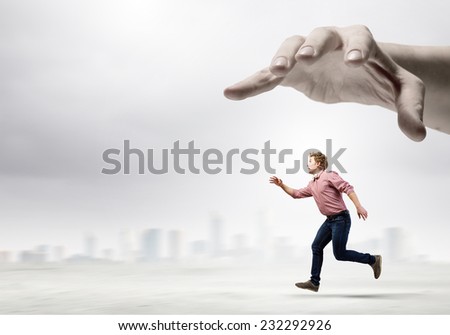 Young man in casual running away from big hand