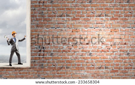 Businessman in helmet hammering nail in brick wall