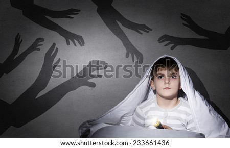 Little scared boy in bed under blanket with flashlight