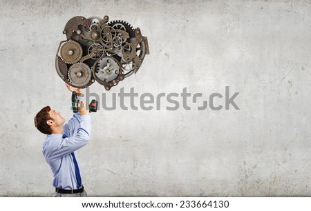 Young businessman using drill to fix gear mechanism