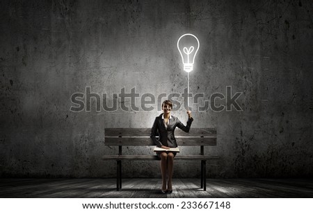 Young smiling businesswoman sitting on bench with book on knees