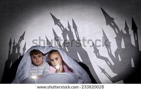 Two little kids with flashlight under blanket