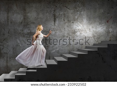 Young woman in white long dress stepping up the staircase